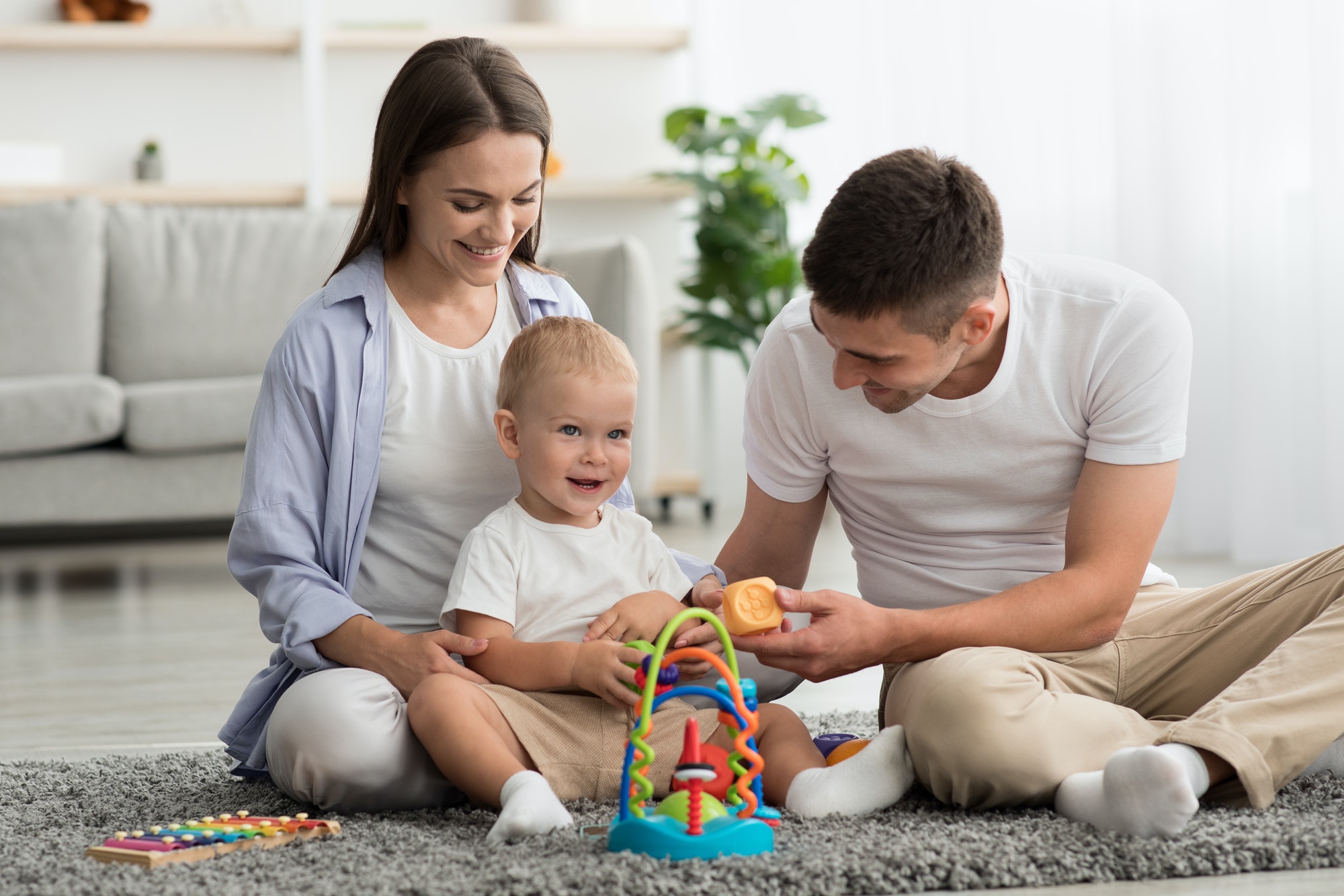 Happy Parents And Adorable Infant Baby Playing With Development Toys At Home